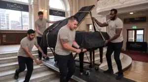 Team of movers carefully transporting a grand piano inside a historic building.